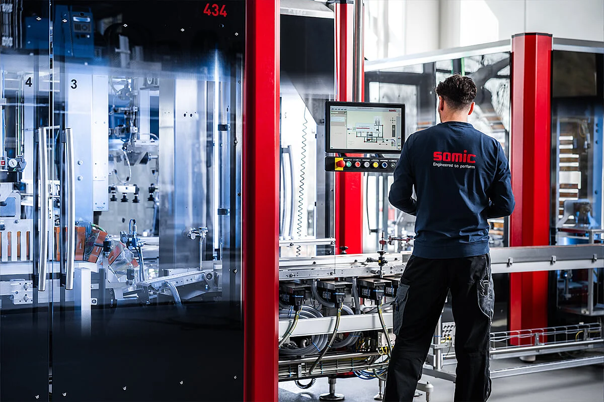 A SOMIC employee stands in front of the HMI of a SOMIC 434 cartoning machine